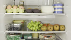 Three refrigerator shelves full of various foods, including grapes, milk and eggs among others.